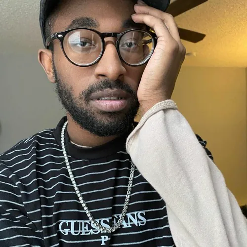 Lil Gohan wearing glasses and a striped shirt with one hand against his face.